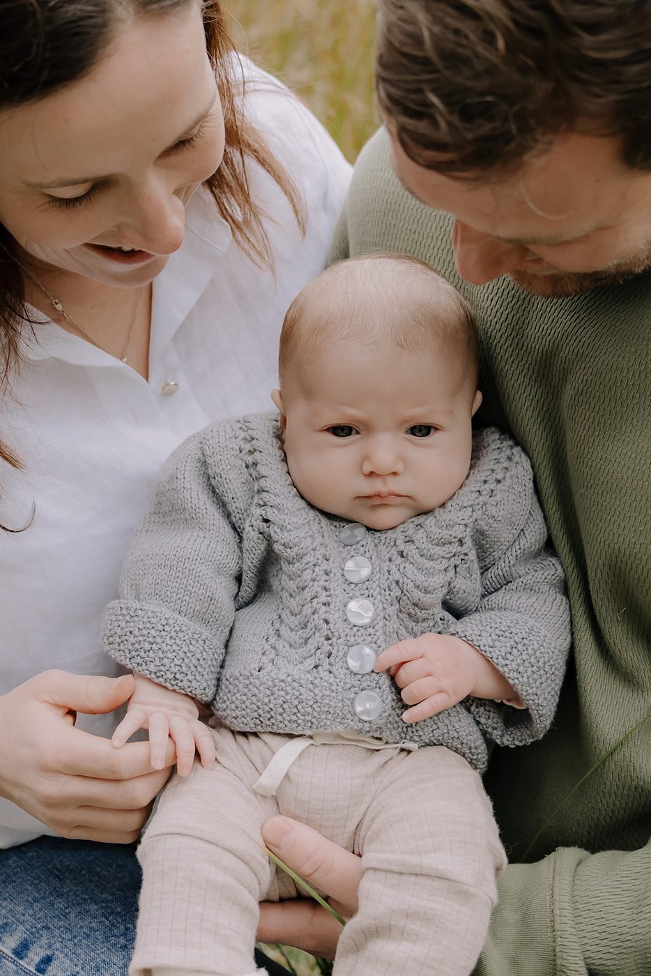 A parent holding a pēpi wearing a hand-knitted cardigan